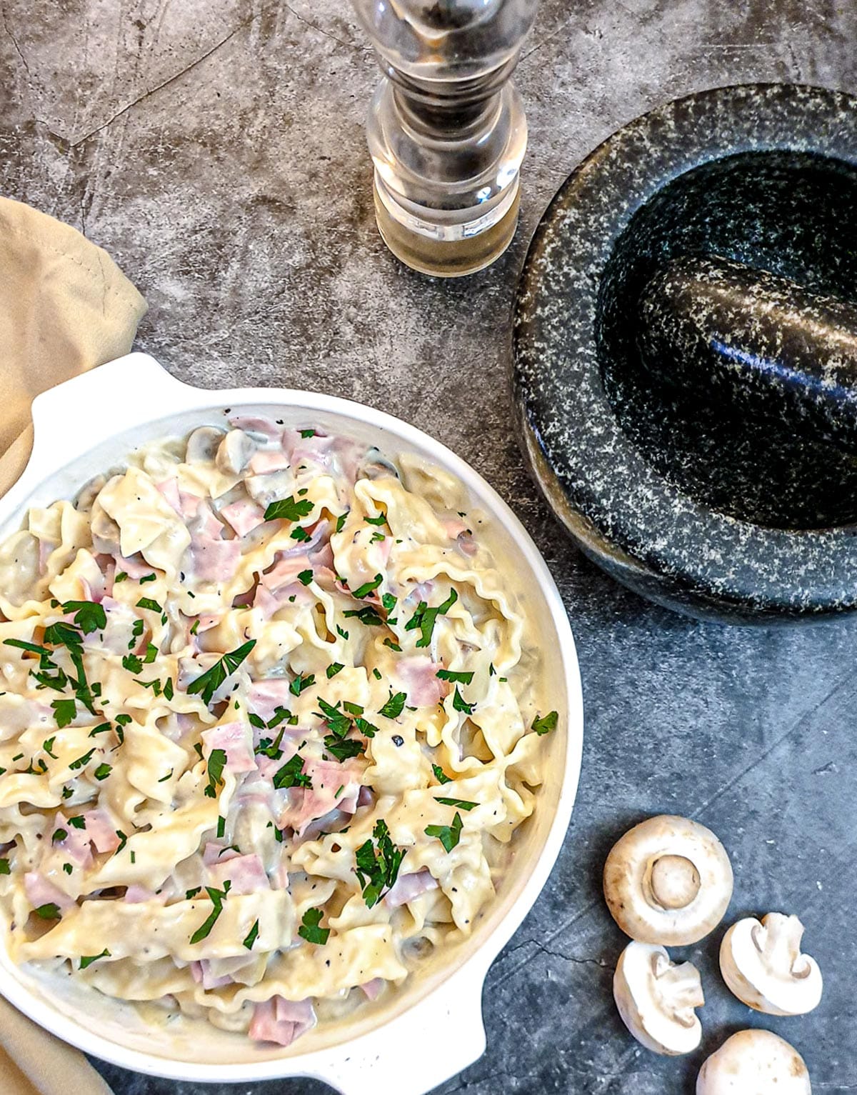 A dish of ham and mushroom tagliatelle on a table next to a pestle and mortar.