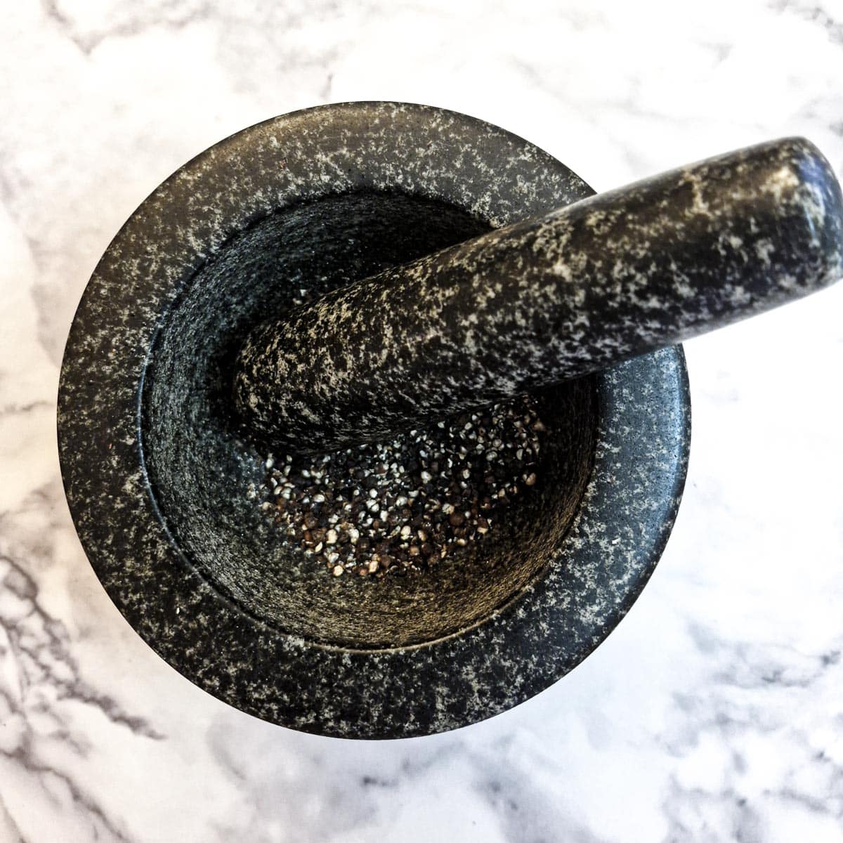 Black peppercorns being crushed in a pestle and mortar.
