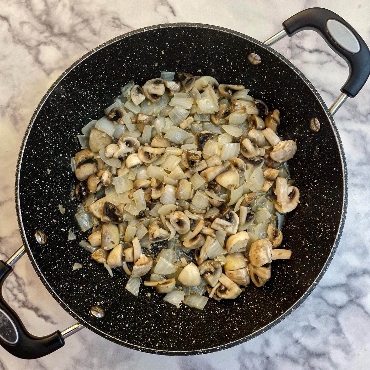Chopped mushrooms softening with onions in a frying pan.