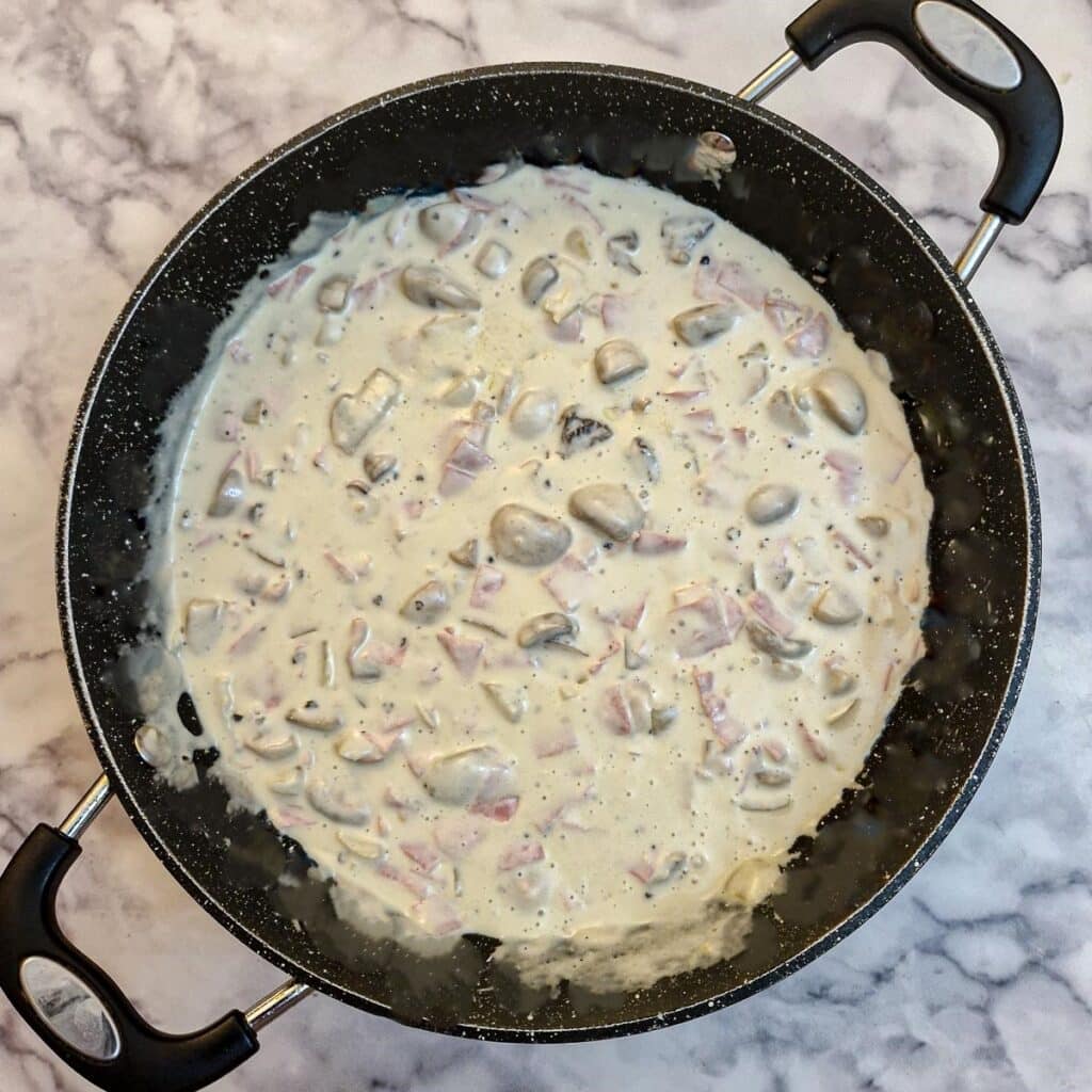 Thickened ham and mushroom black pepper sauce in a frying pan.