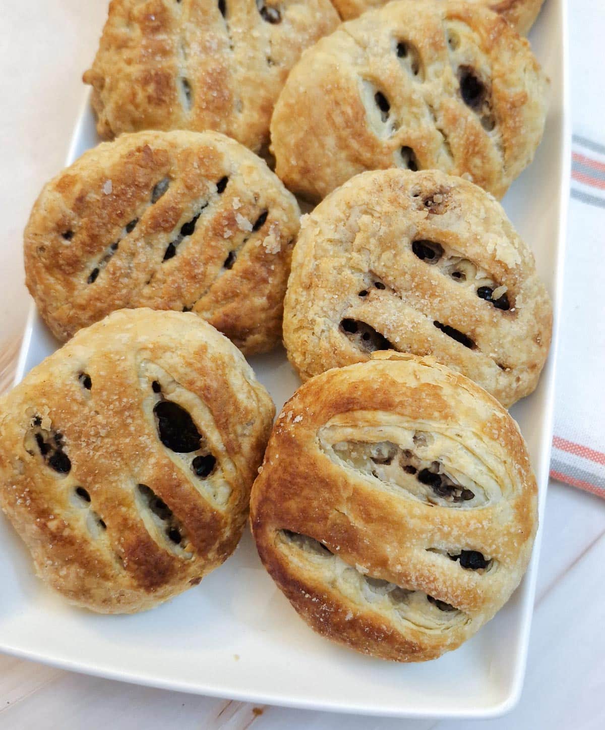 Close up of 6 eccles cakes arranged on a white rectangular plate.