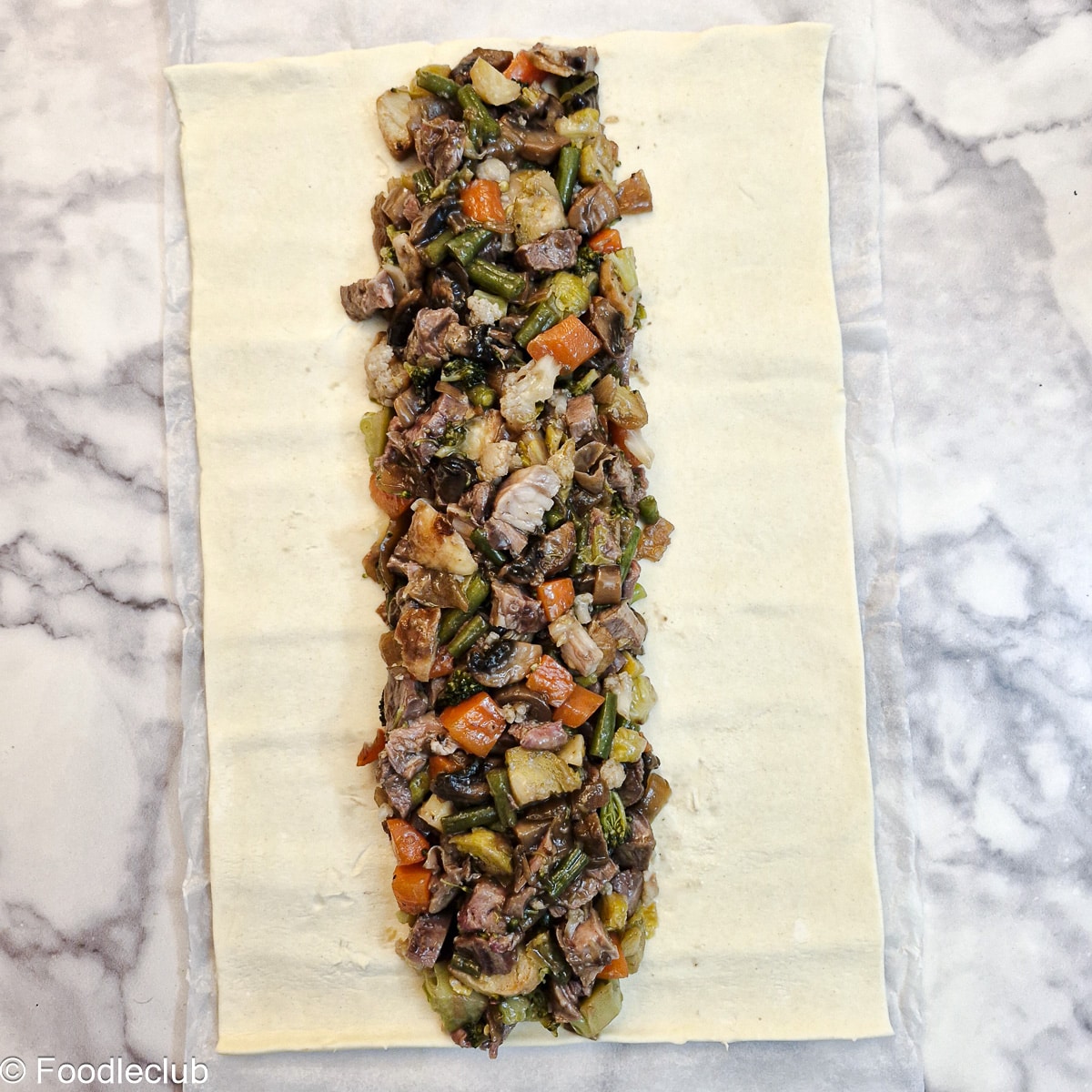 Chopped leftover meat and vegetables arranged in the centre of a sheet of puff pastry.