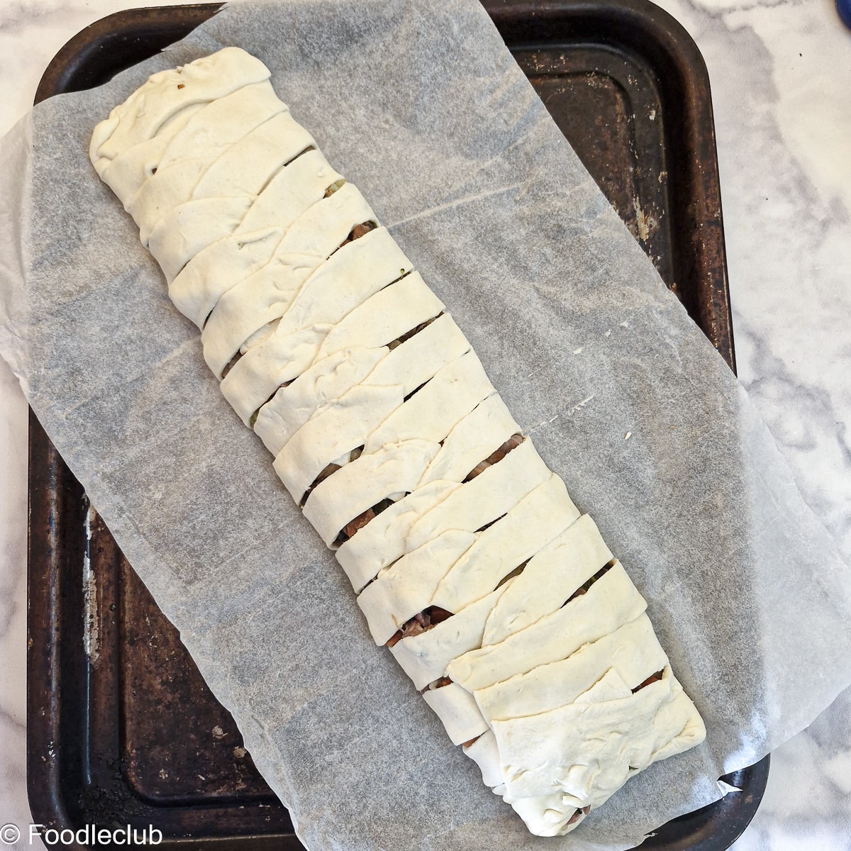 An assembled puff pastry braid arranged on baking paper on a baking sheet.