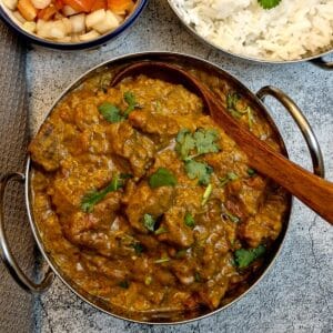 A balti dish of beef madras curry with a wooden serving spoon.