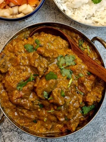 A balti dish of beef madras curry with a wooden serving spoon.