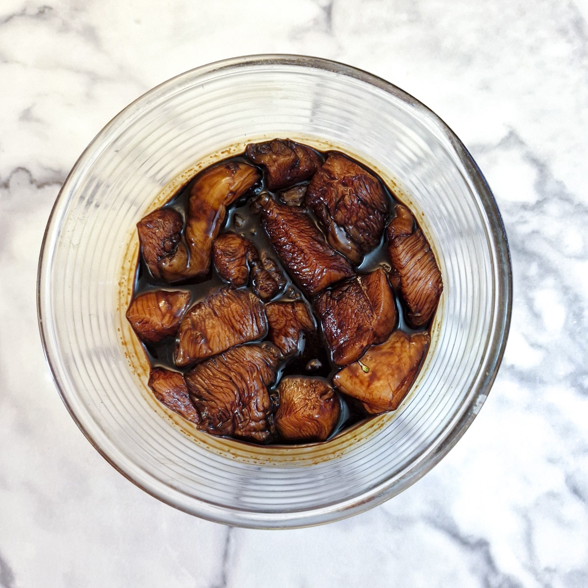 Pieces of chicken marinating in a mixture of soy sauce and cornflour in a glass bowl.