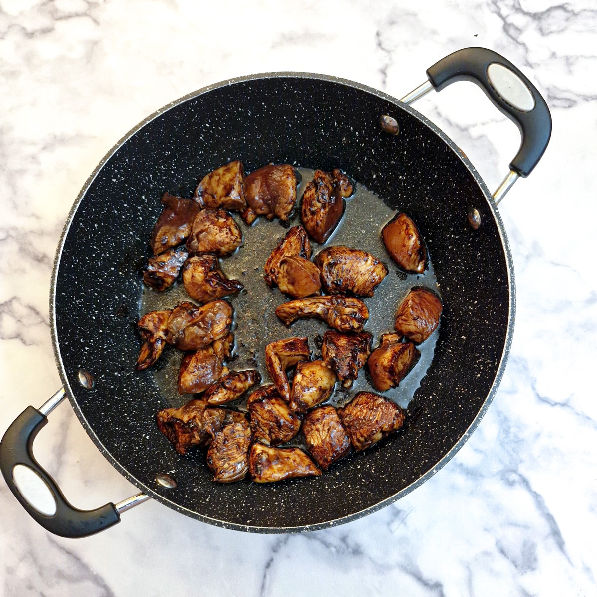 Pieces of chicken browning in a frying pan.