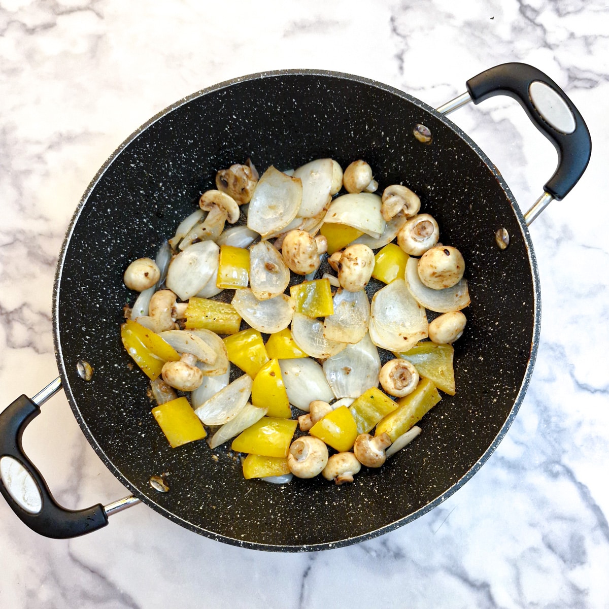 Onions, mushrooms and peppers frying in a frying pan.