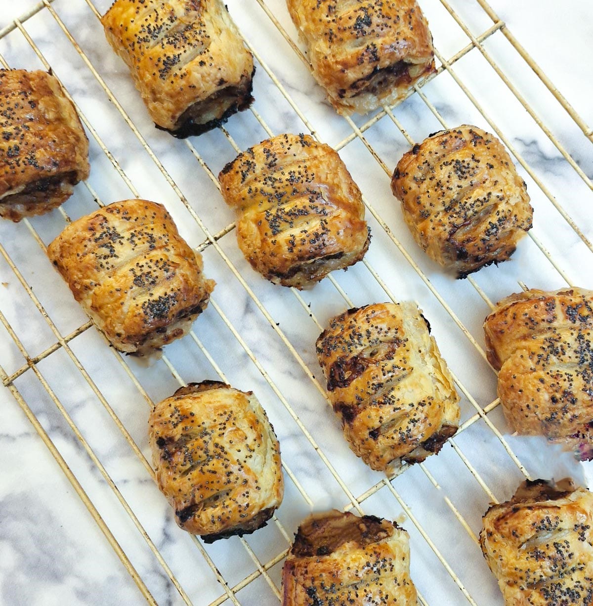 A wire cooling rack with 12 sausage rolls arranged on it.