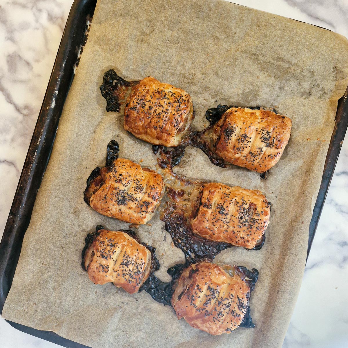 6 golden brown baked stilton, pear and walnut sausage rolls on a baking tray.