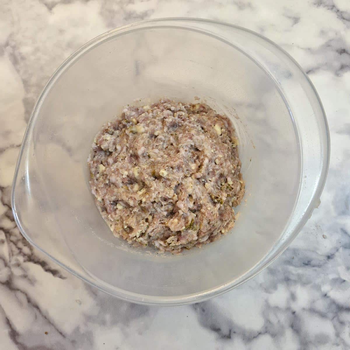 A plastic mixing bowl containing a ball of filling for sausage rolls.