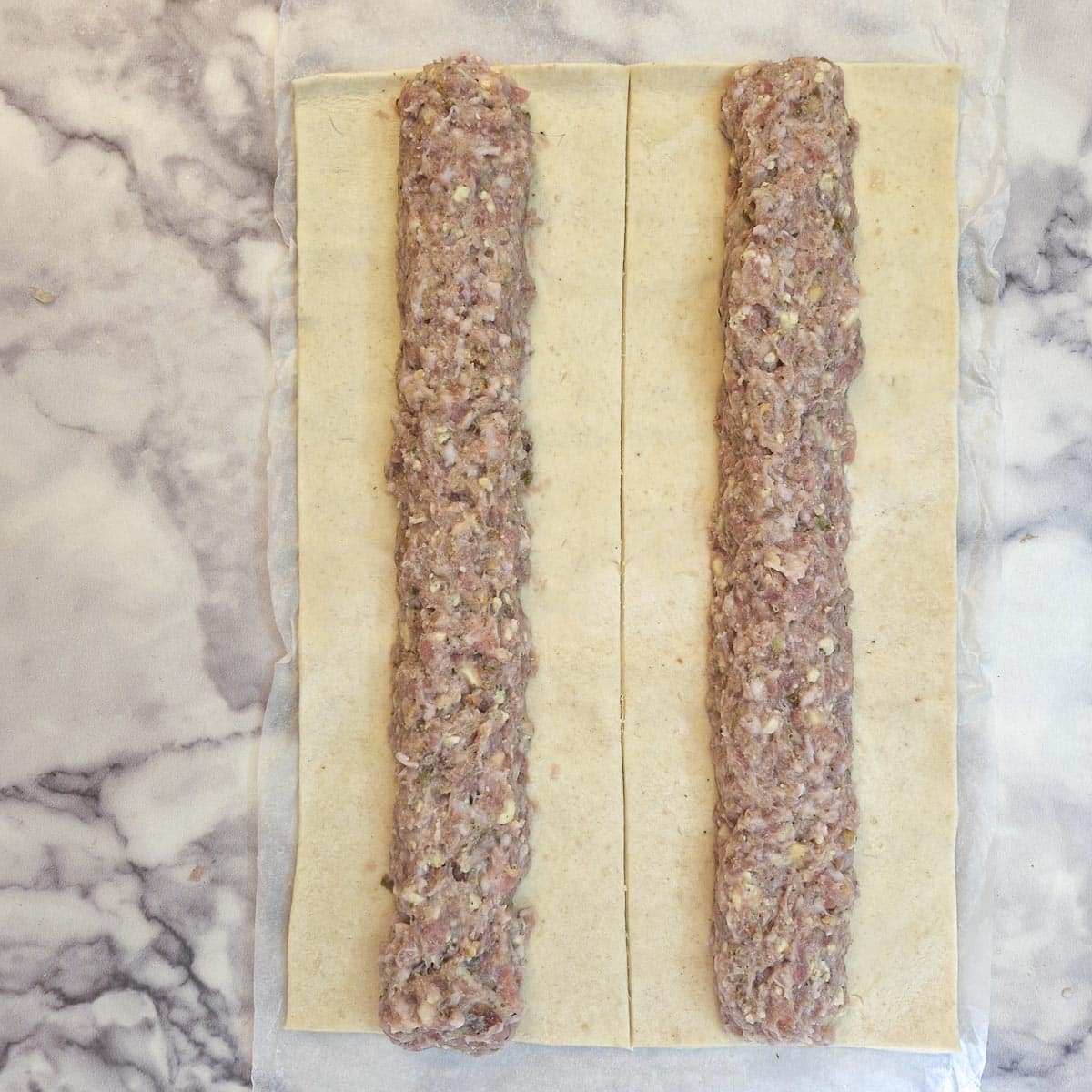 Sausage roll filling formed into two long sausages and laid on puff pastry.