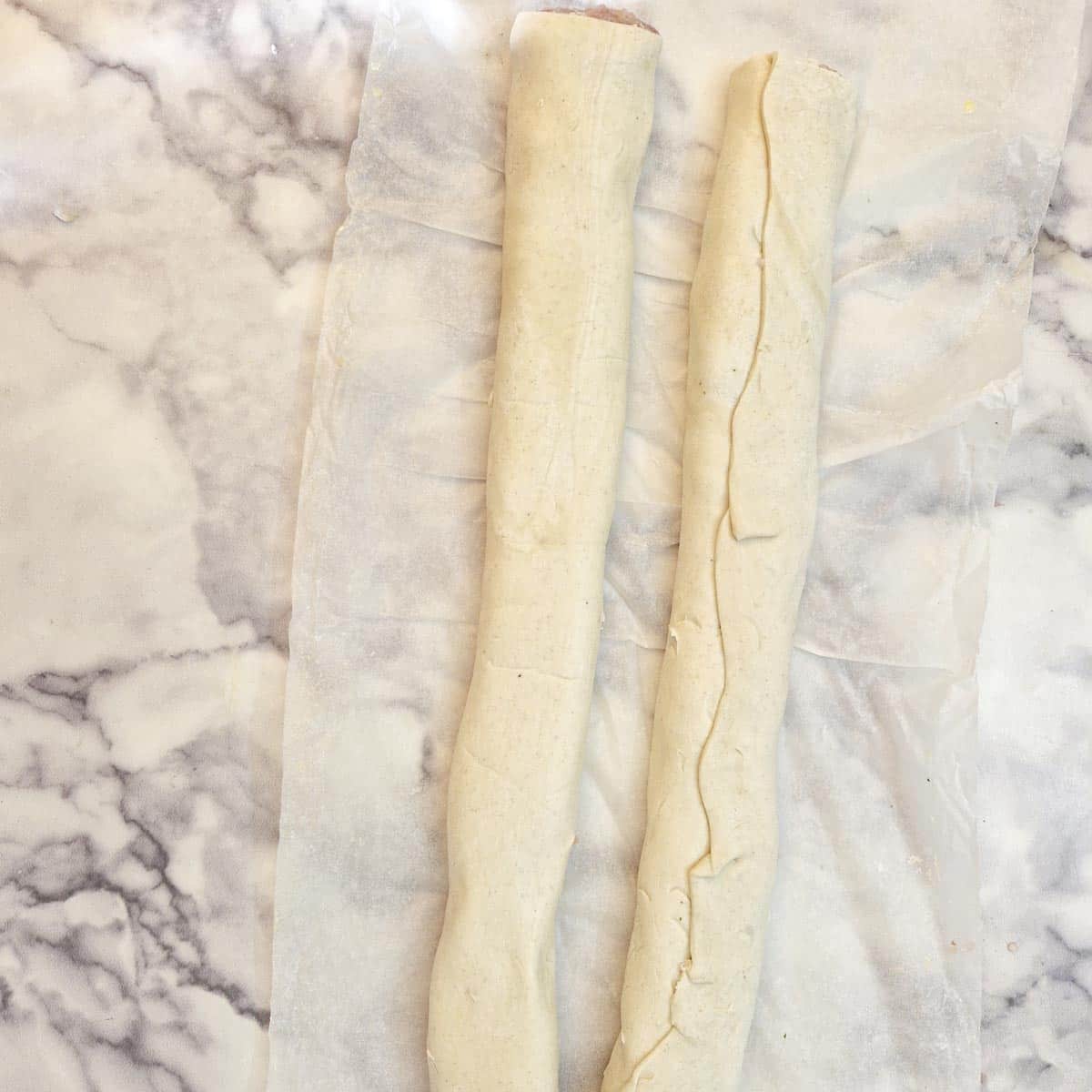 Two long (uncut) uncooked sausage rolls.