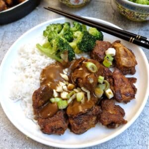 Satay chicken with rice and broccoli covered with satay sauce on a white plate with chopsticks.