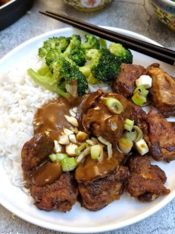 Satay chicken with rice and broccoli covered with satay sauce on a white plate with chopsticks.