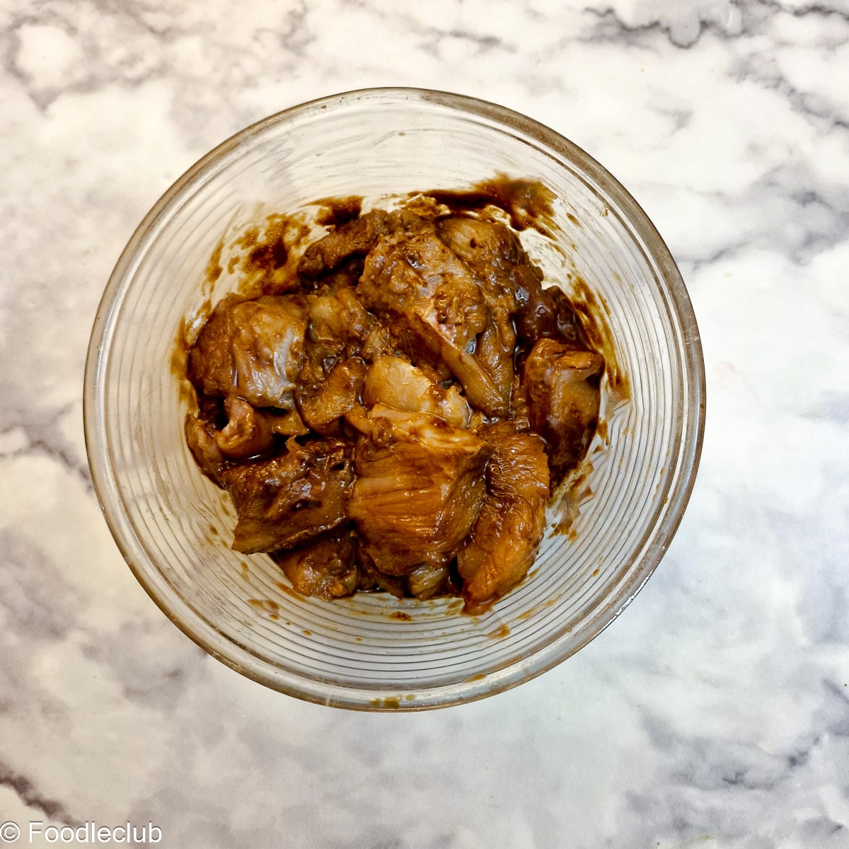 Chicken pieces marinating in soy sauce and cornflour in a glass bowl.