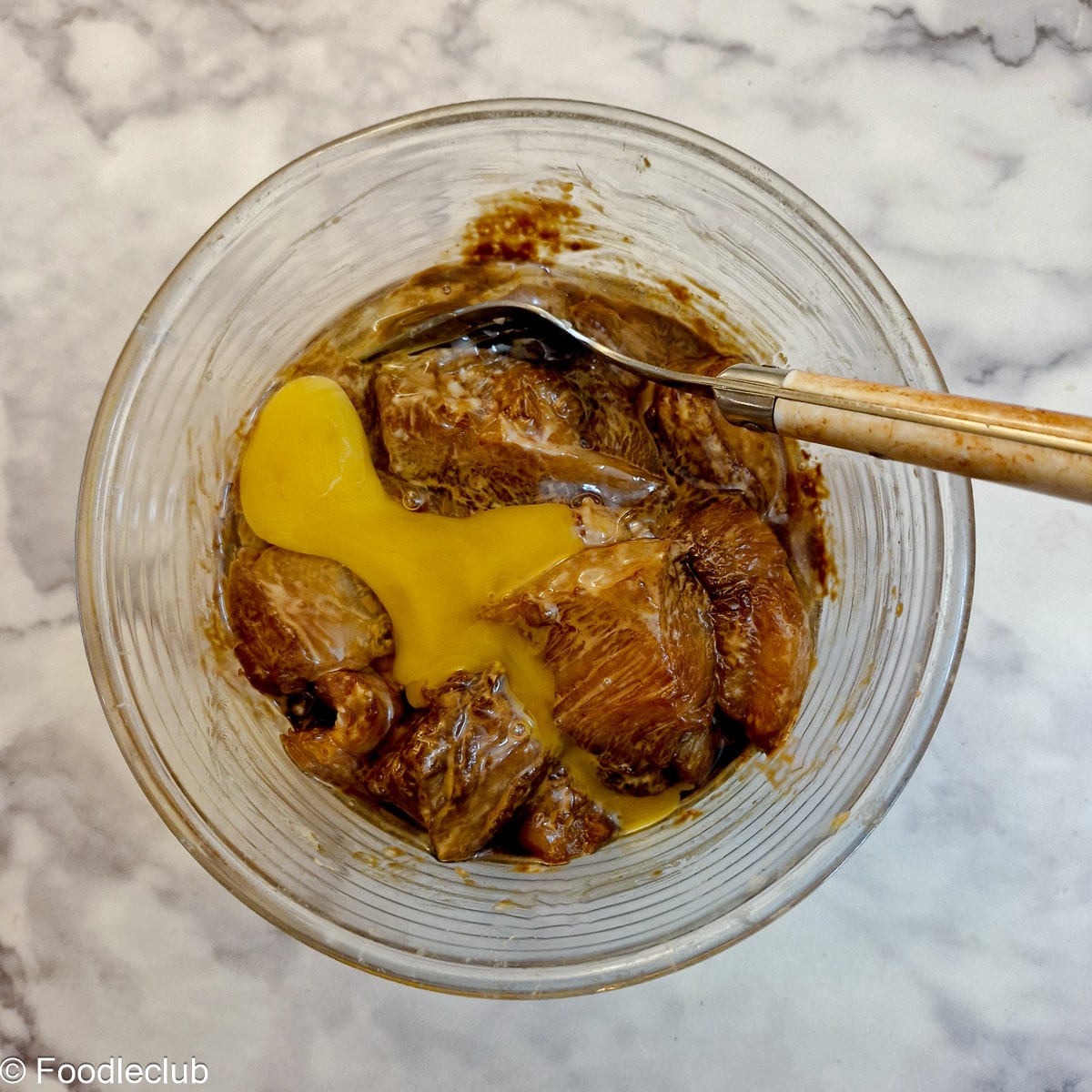 An egg added to chicken pieces in a glass bowl.