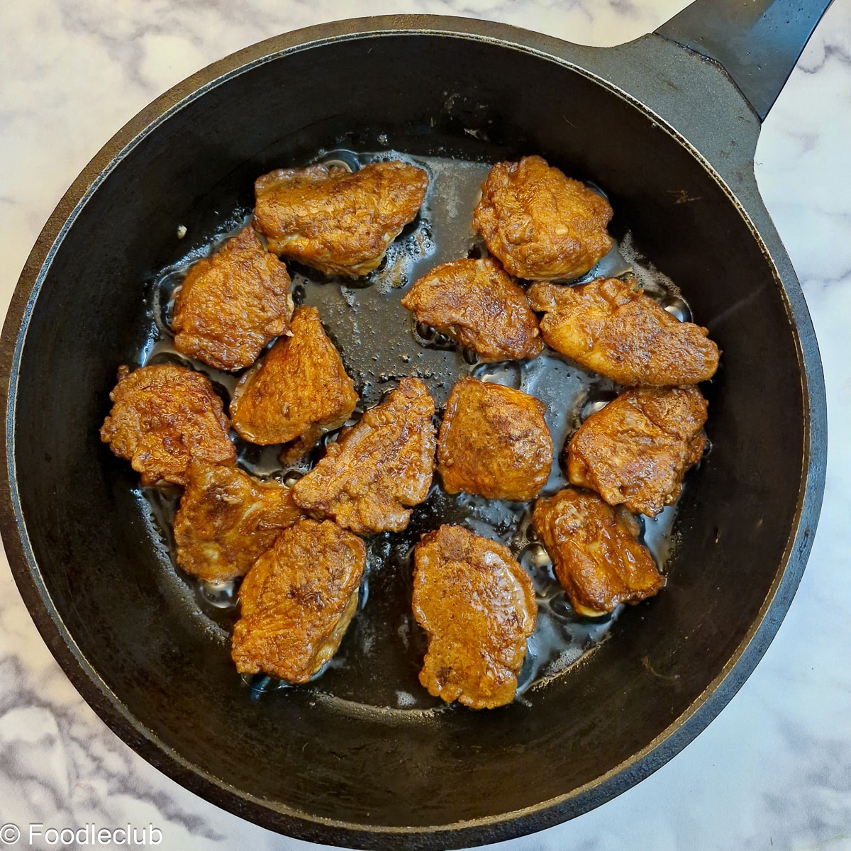 Browned chicken pieces in a frying pan.