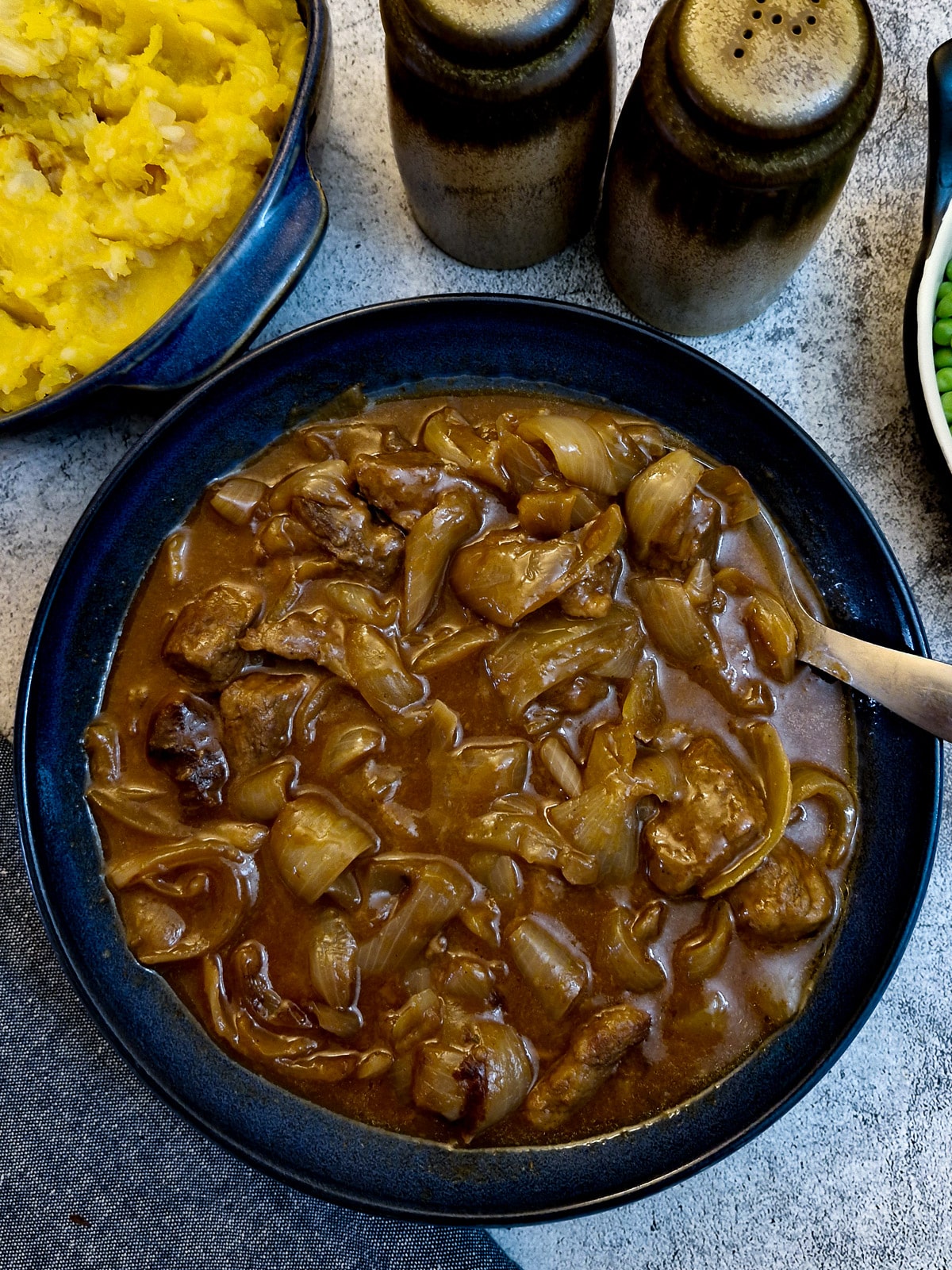 A blue serving dish of braised steak and onions in a rich gravy.