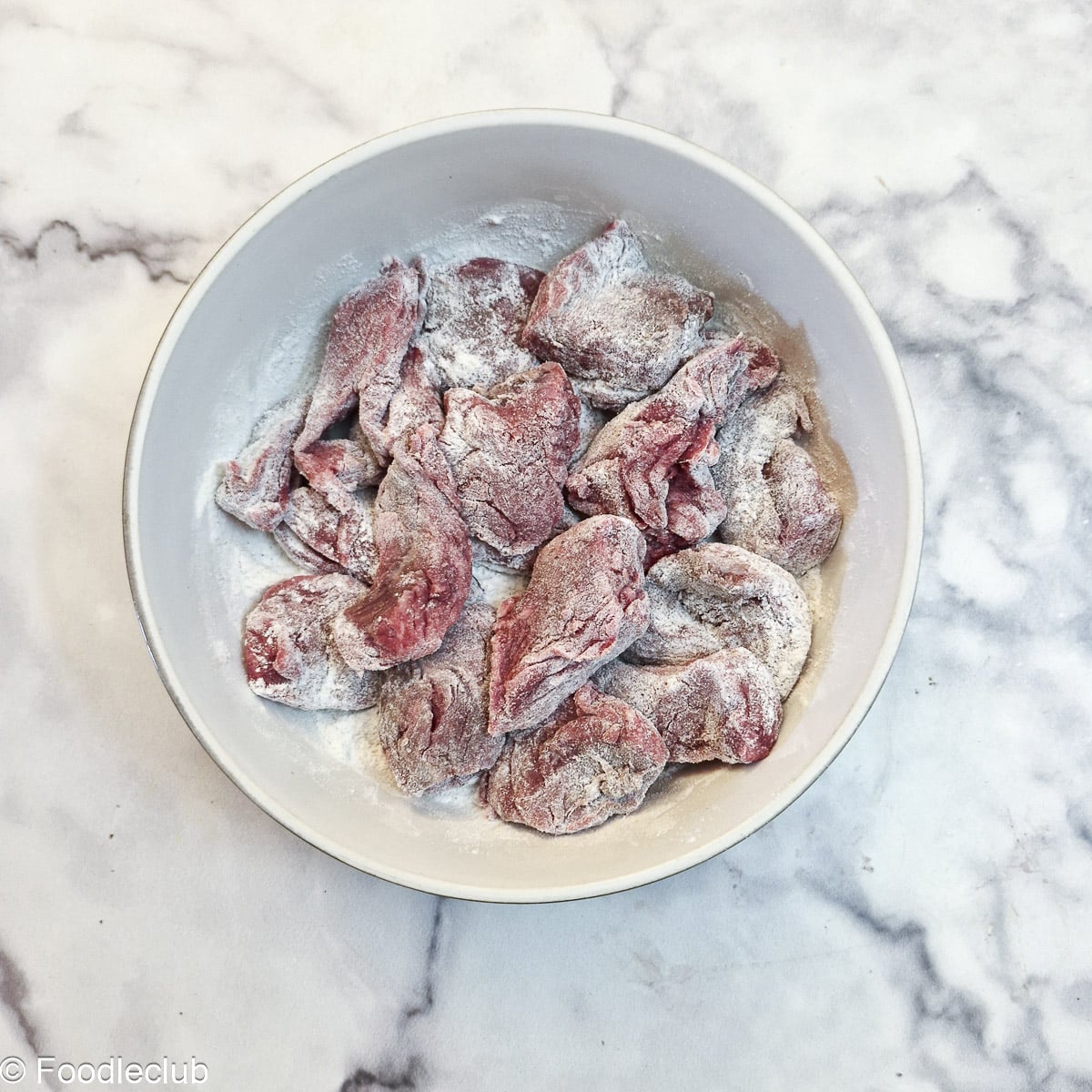 Pieces of steak coated in flour in a small white bowl.