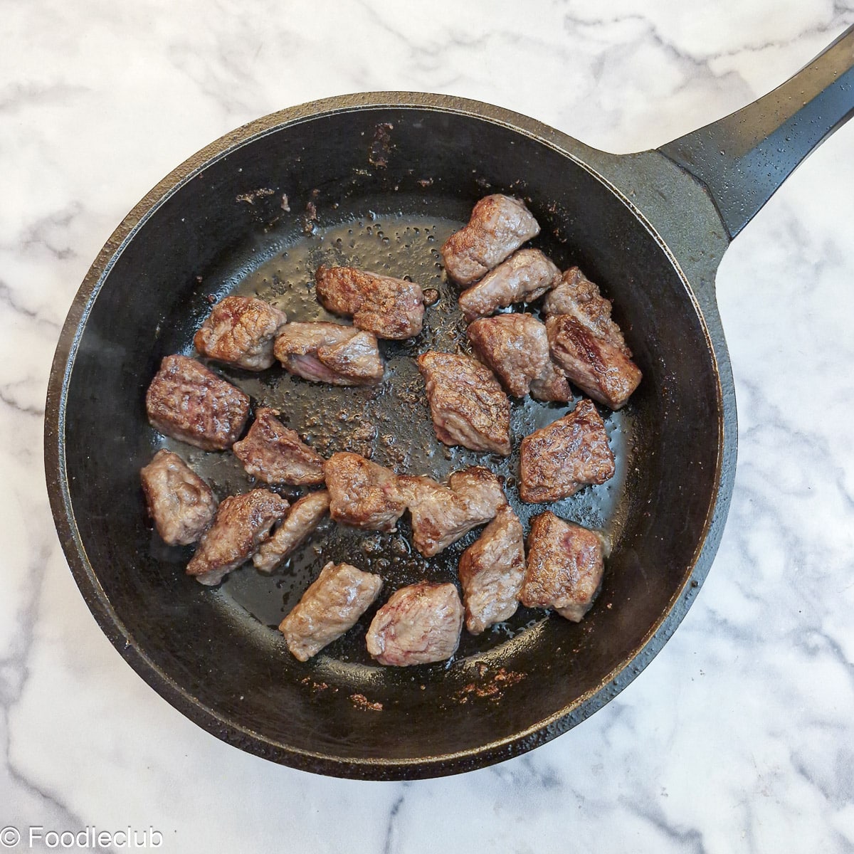 Pieces of steak browning in a frying pan.