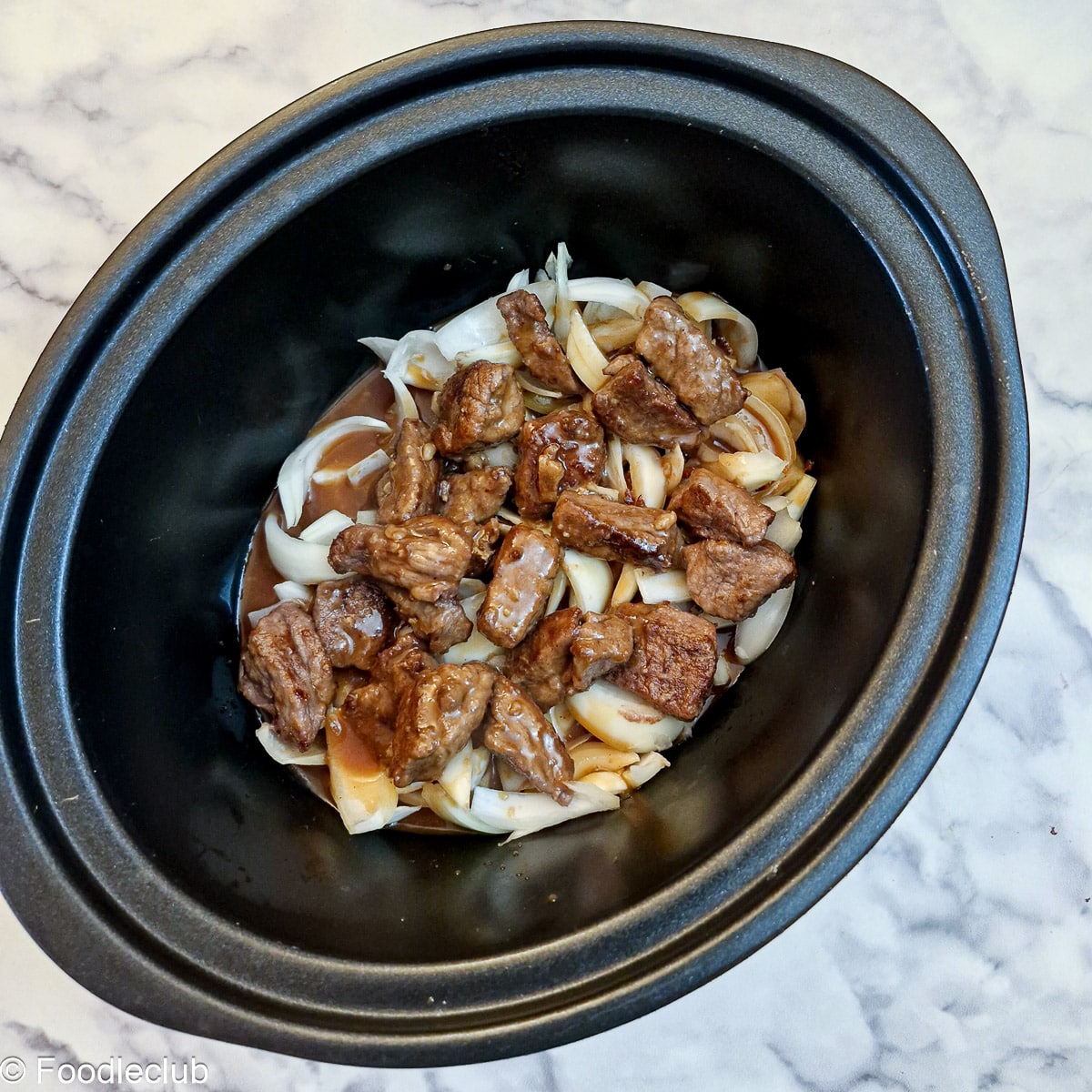 Stock combined with onions and steak in the inner liner of a slow cooker.
