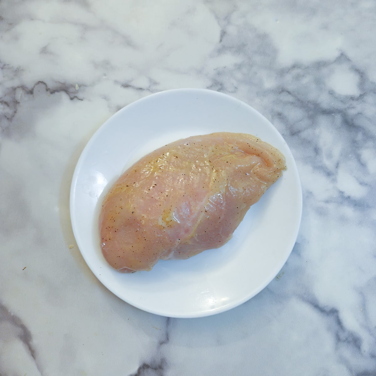 A raw chicken breast coated with honey and mustard on a white plate.