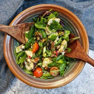 A bowl of chicken and bacon salad with a set of salad servers in a brown bowl.