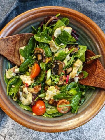 A bowl of chicken and bacon salad with a set of salad servers in a brown bowl.