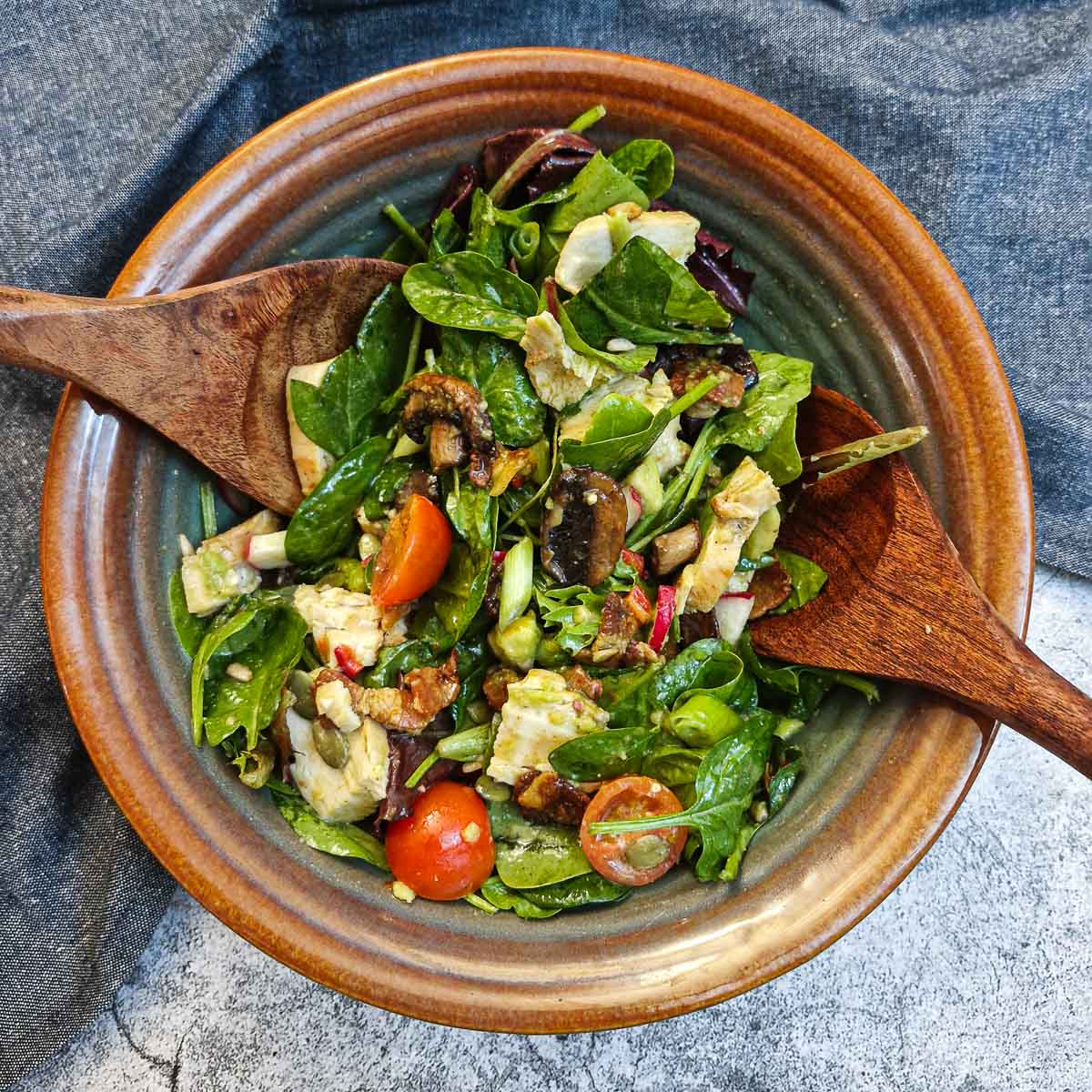 A bowl of chicken and bacon salad with a set of salad servers in a brown bowl.