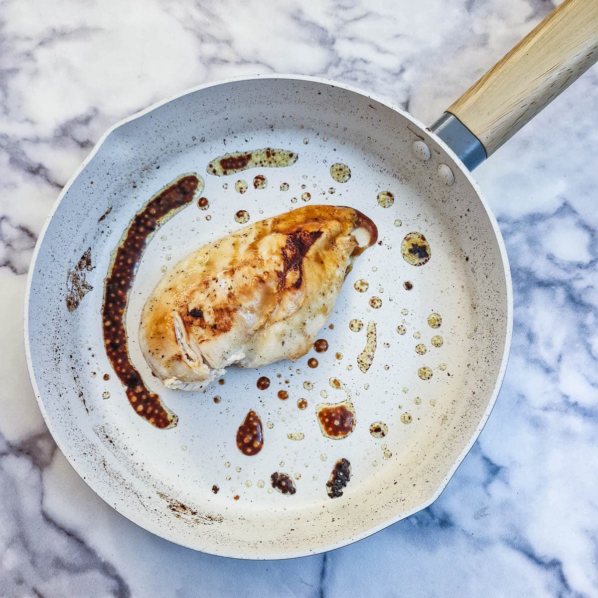 A browned chicken breast in a white frying pan.