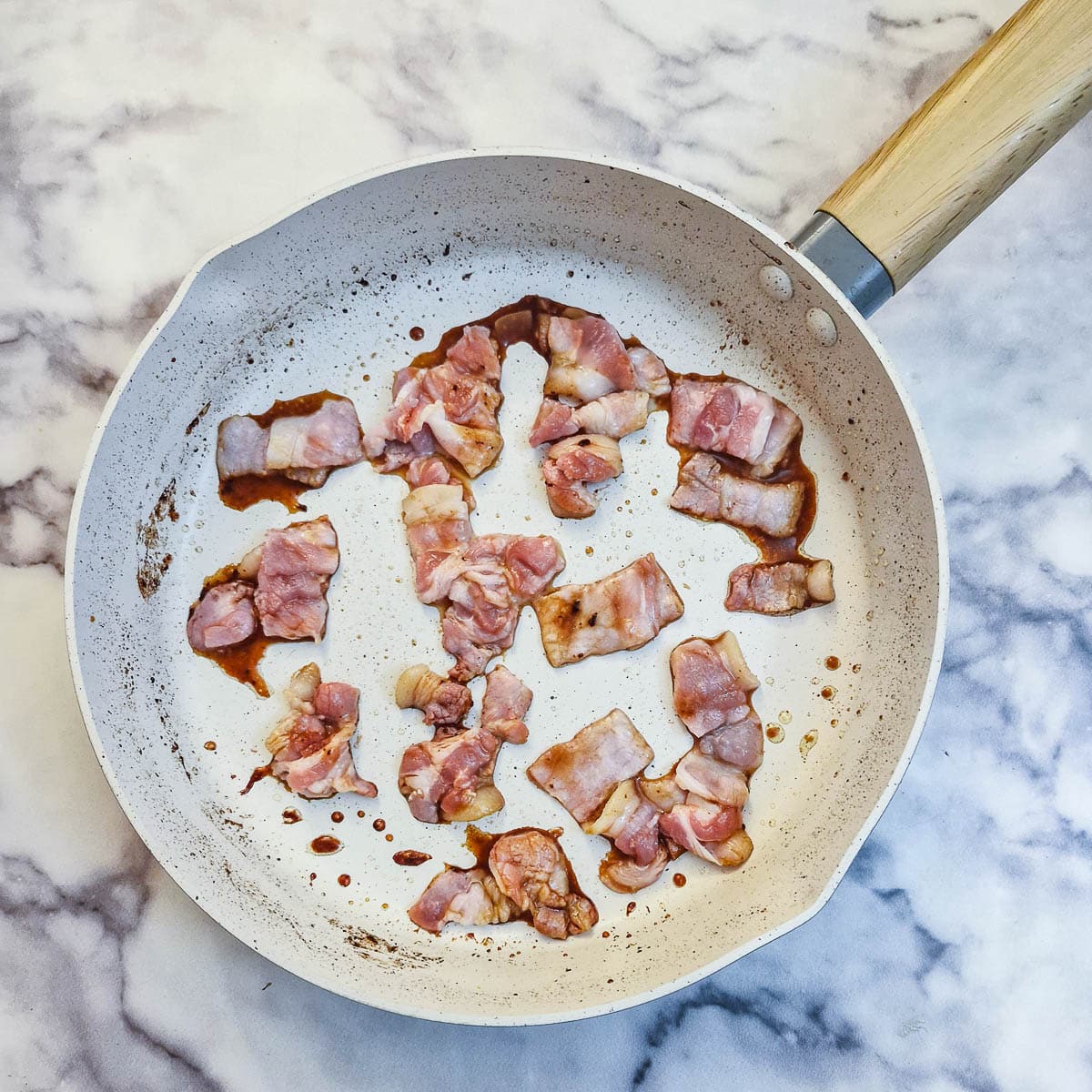 Bacon pieces in a white frying pan.