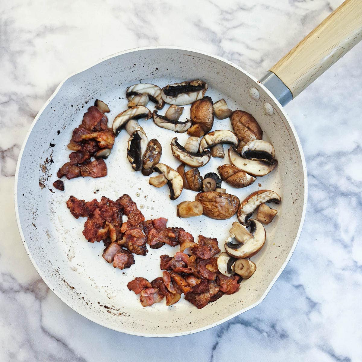 Sliced mushrooms added to bacon in a pan.