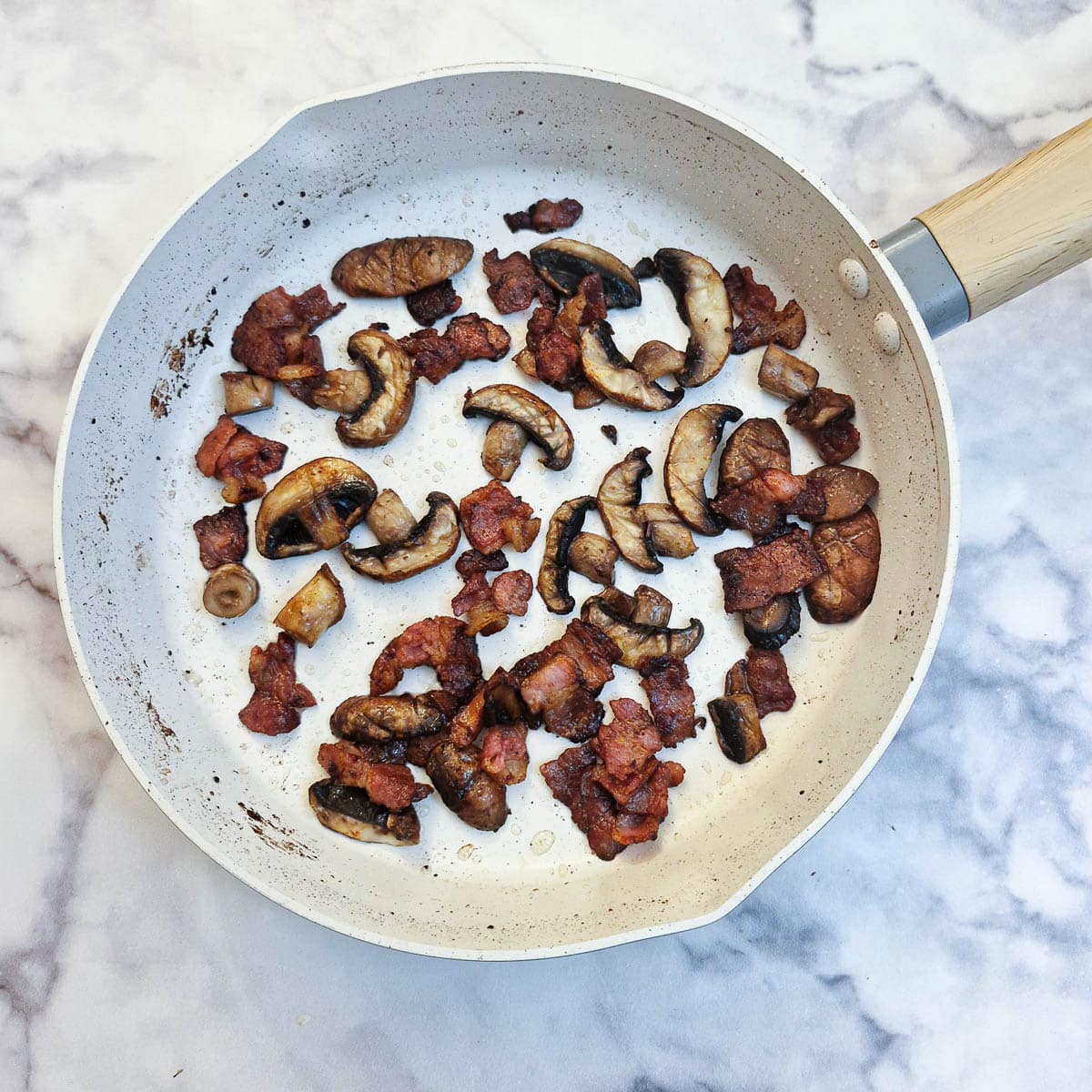 Fried mushrooms and bacon pieces in the pan.