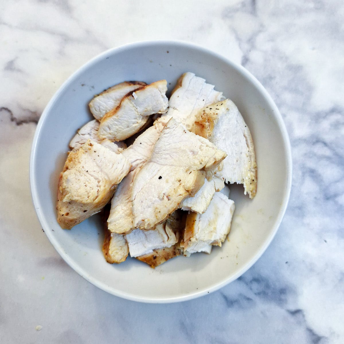 Sliced cooked chicken breasts in a small white bowl.