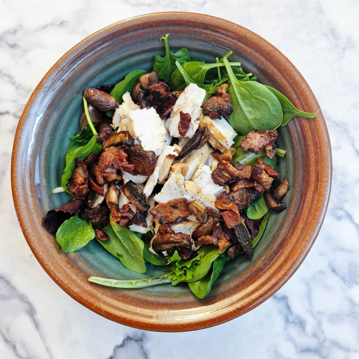 Salad leaves with chicken, mushrooms and bacon in a brown salad bowl.