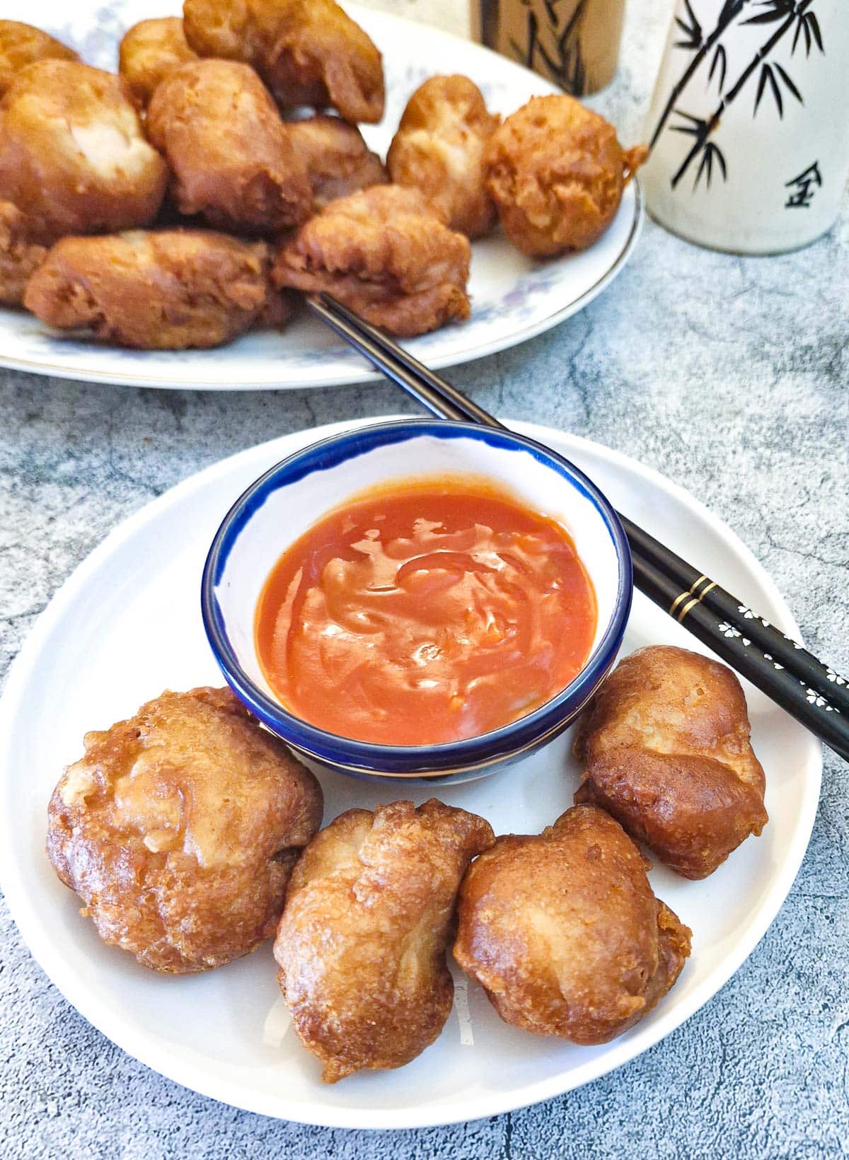 4 crispy chicken balls on a white plate with a dish of sweet and sour sauce.