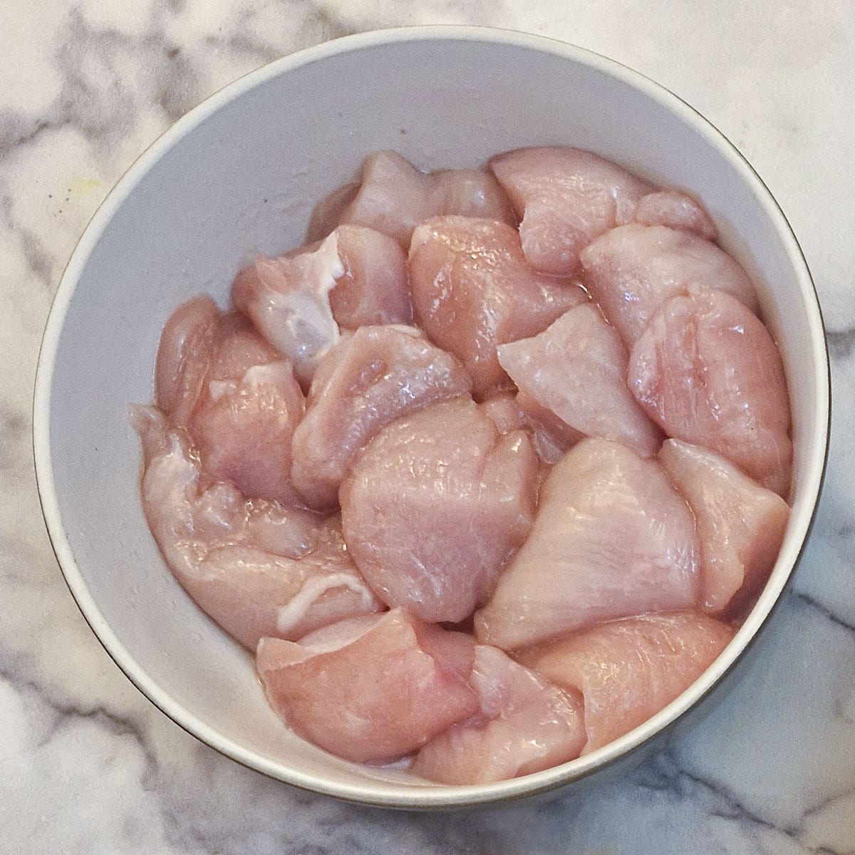 Cubes of chicken breast in a white dish.