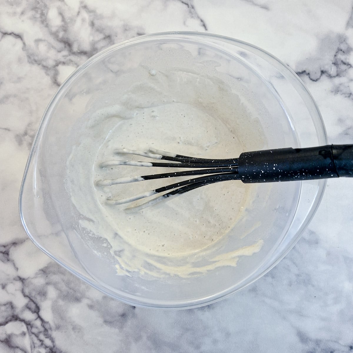 Batter being whisked in a mixing bowl with a balloon whisk.