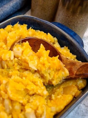 Close up of a blue serving dish of rumbledethumps with a wooden serving spoon.
