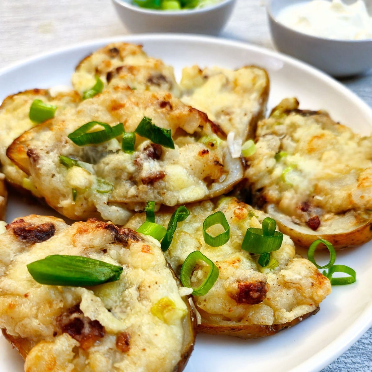 Stuffed potato skins garnished with chopped spring onions on a white plate.
