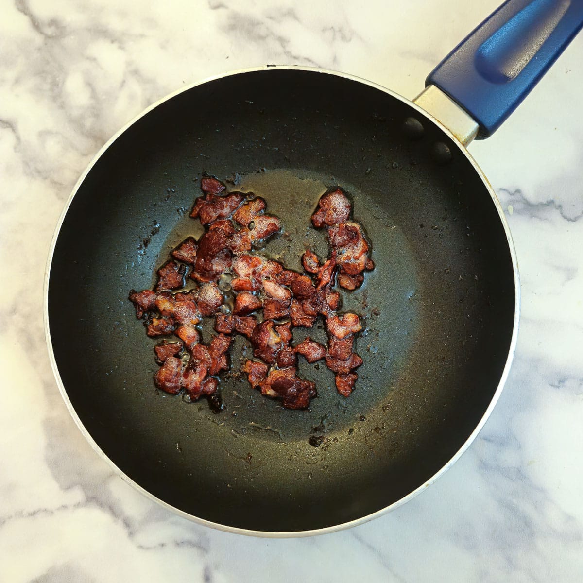 Bacon pieces frying in a black frying pan.
