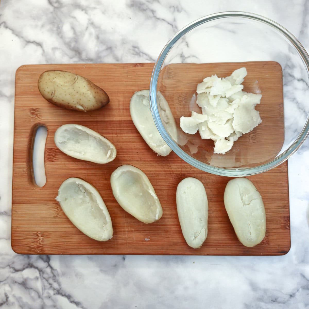 Baked potatoes cut in half with the insides scooped into a bowl.