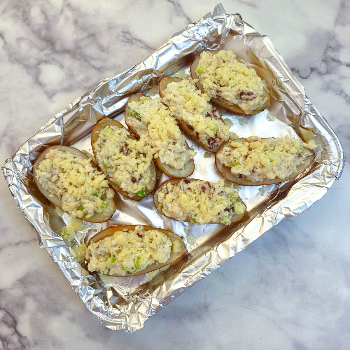 Potato skins stuffed with filling and covered with grated cheese on a baking tray.