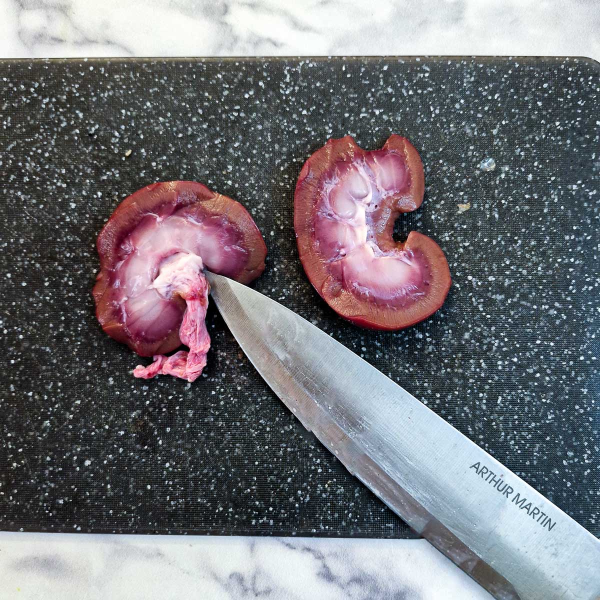 A lamb kidney cut in half showing how to remove the fatty core with a knife.