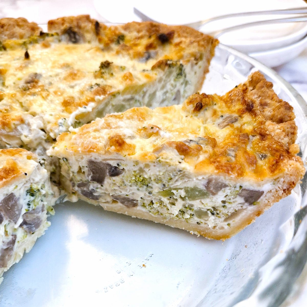 Side-on slices of cheese and broccoli quiche on a glass serving dish, showing the inside of the quiche.