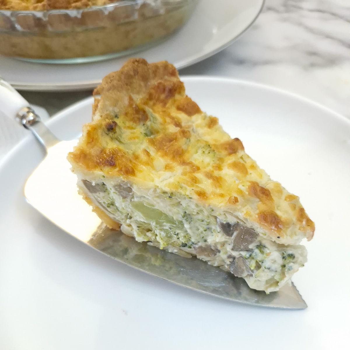 A slice of cheese and broccoli quiche being placed onto a white plate.