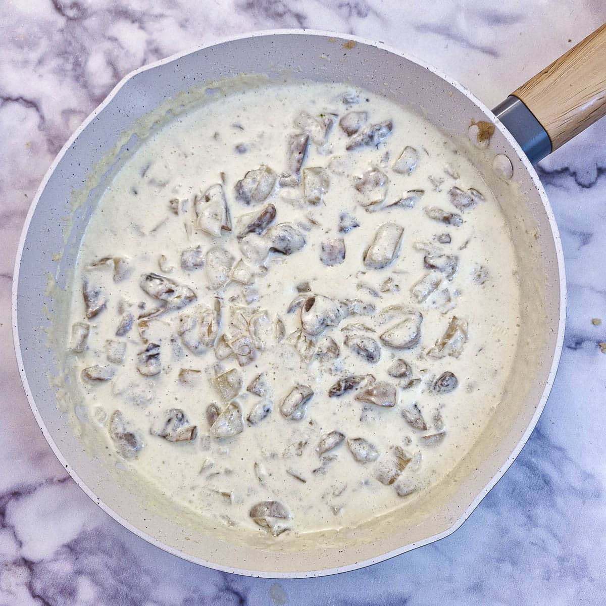 Cream and milk mixed with mushrooms and onions in a frying pan.