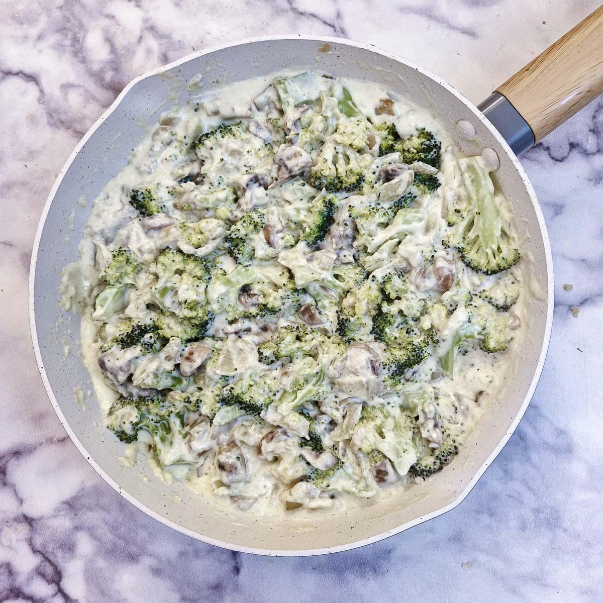 Steamed broccoli added to the quiche filling in a frying pan.