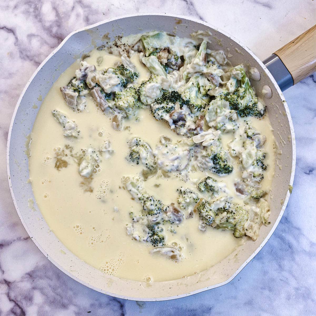 Beaten egg and milk poured into the quiche filling in a frying pan.